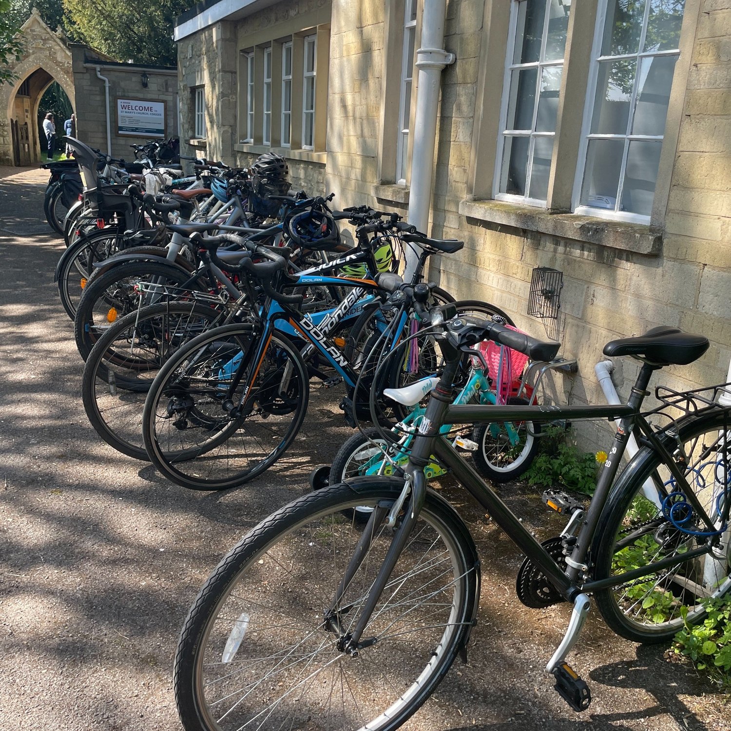 Bicycles outside Cogges Church Centre, with the church gate and welcome sign beside it